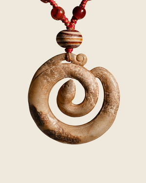 Carved pale stone pendant coiled like a serpent, hung on red cord with red beads and a banded bead.