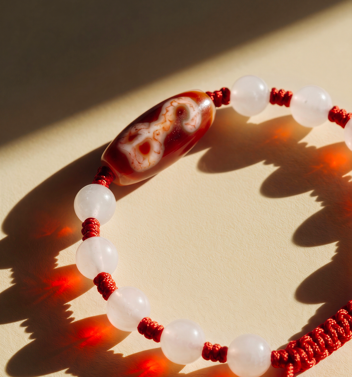 Frosted white bead bracelet on knotted red cord with a red bead bearing a white hook pattern.