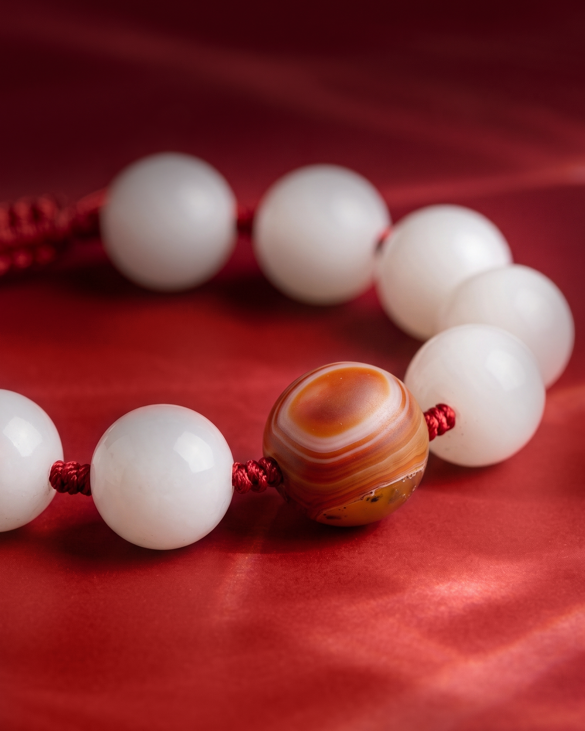 White beads on red cord around a round orange banded bead, on red fabric.