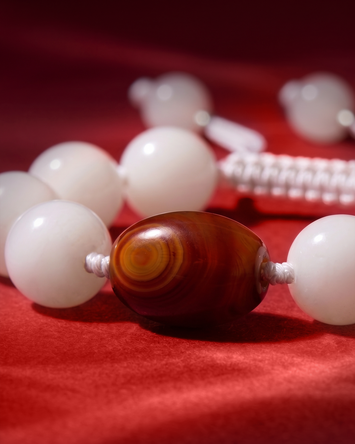 Close-up of an oval red-brown banded bead between white beads on white cord.