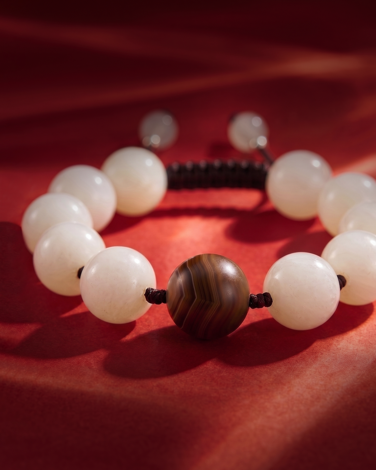 White bead bracelet with a round brown banded center bead on red fabric.