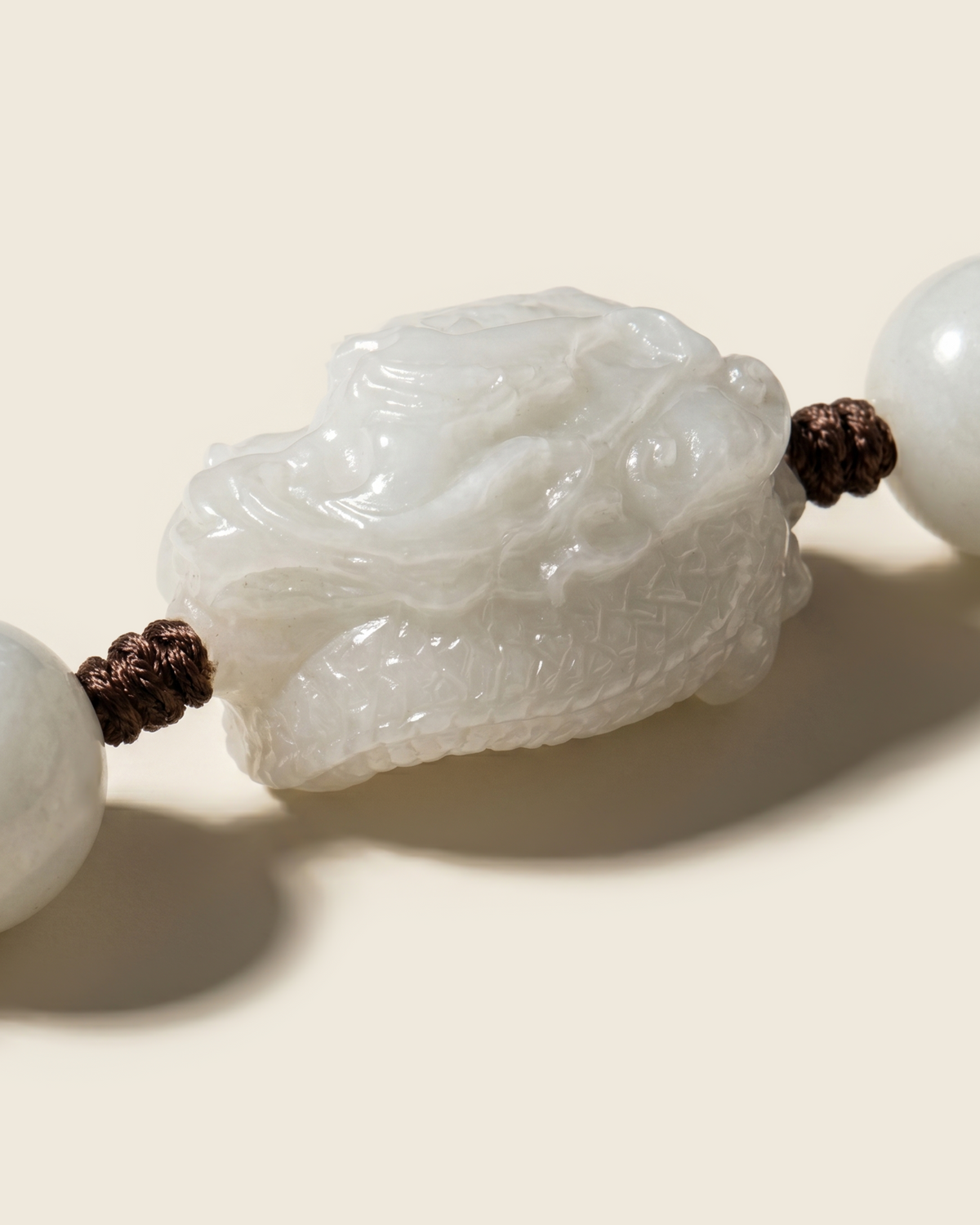 Close-up of a carved white bead between round beads on brown cord.
