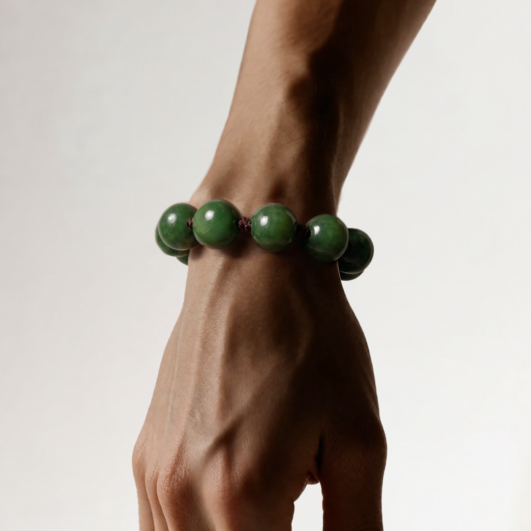 Wrist wearing a bracelet of large round dark green jade beads, against a pale grey backdrop.