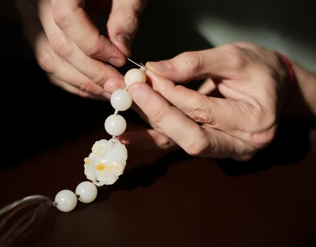 Hands threading white beads and a carved centerpiece onto a cord.