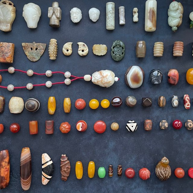 Rows of carved jade, agate, carnelian, amber and Dzi beads laid out on dark cloth.