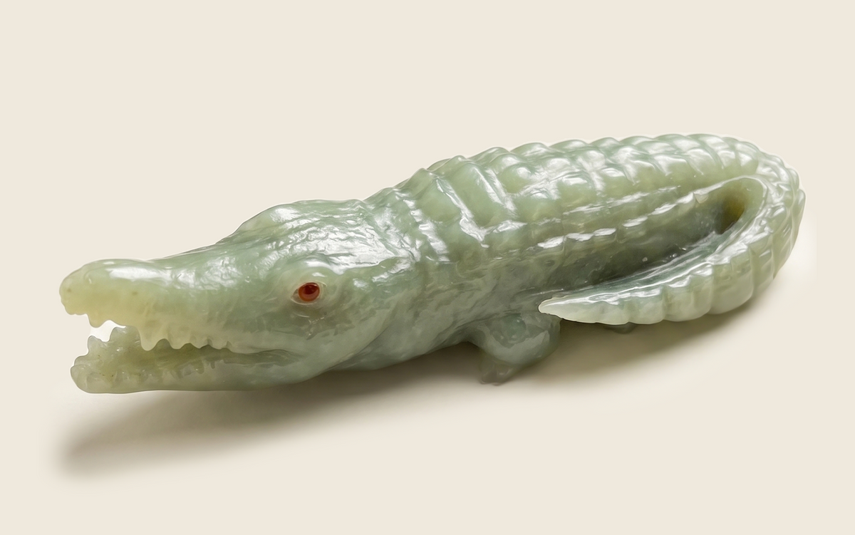 Side view of a pale green carved crocodile with a red eye.