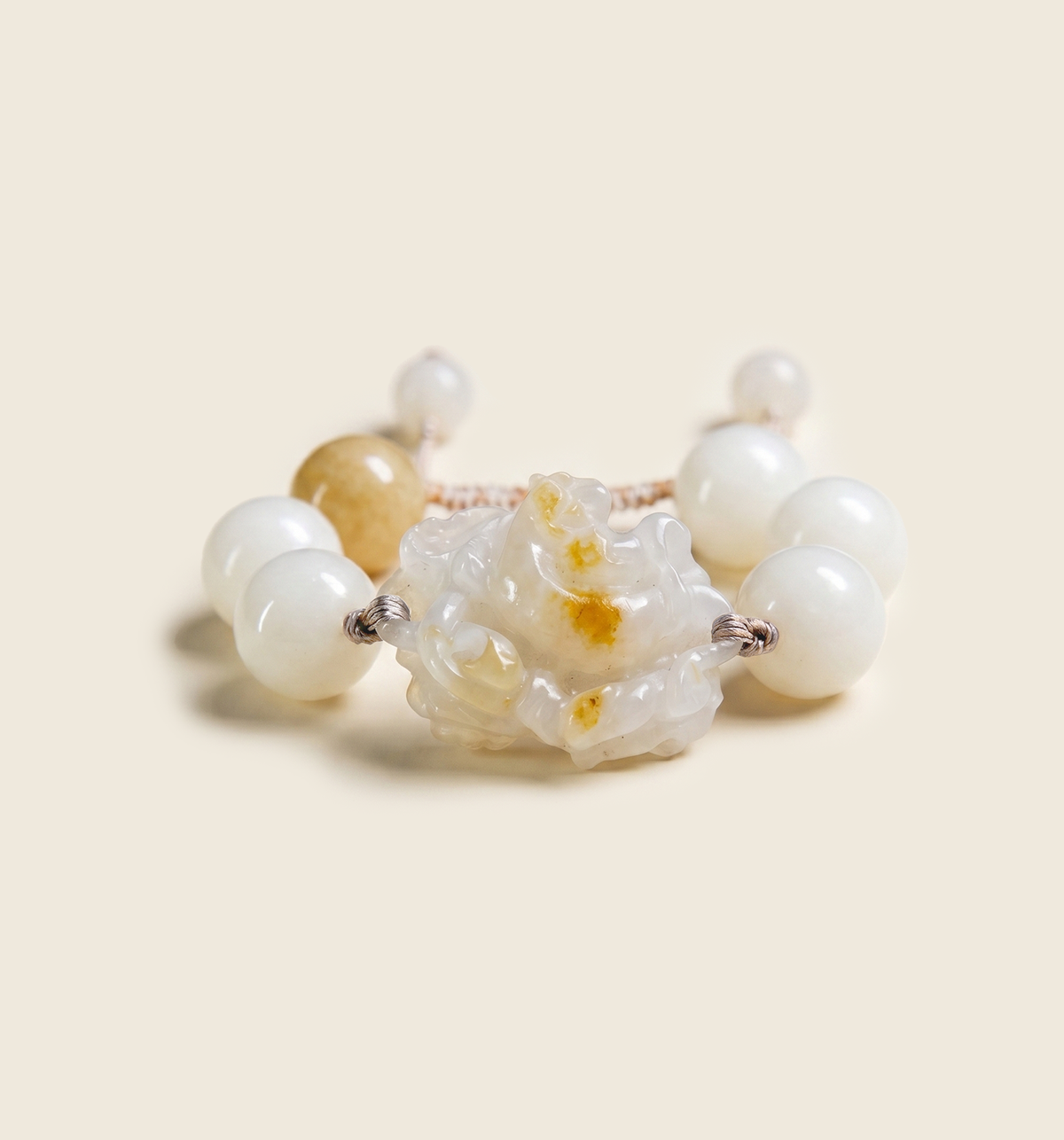 White bead bracelet with a carved white flower centerpiece flecked with gold, on a cream backdrop.