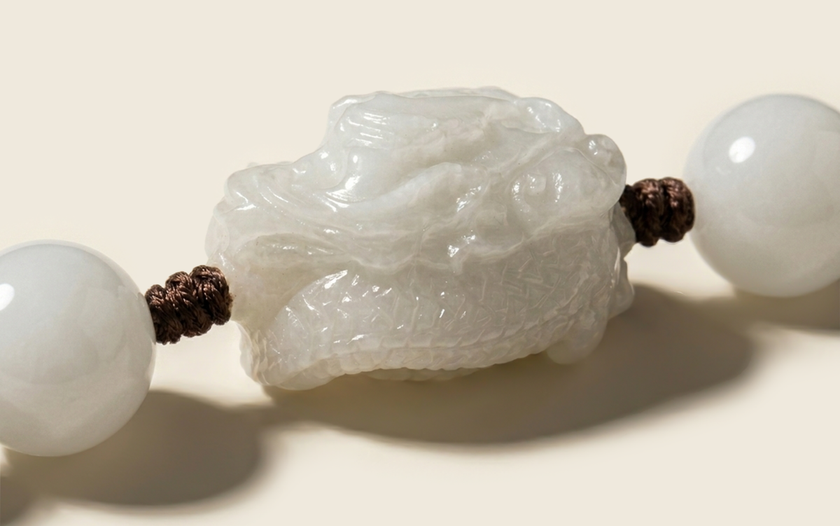 Close-up of a carved white dragon centerpiece between round beads on brown cord.